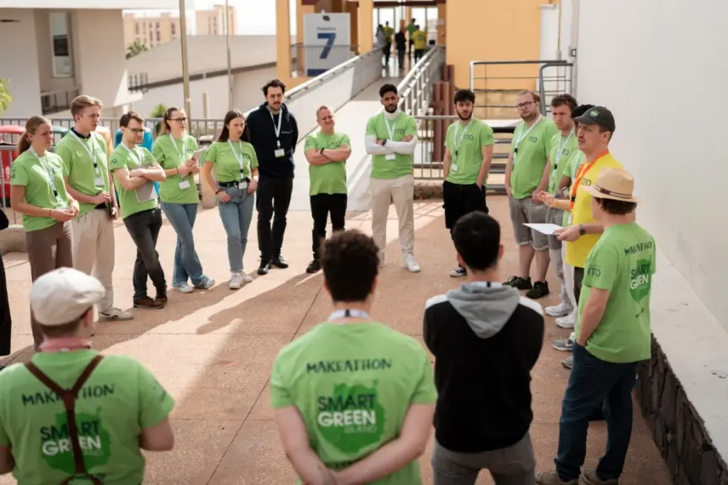 Eine Gruppe von Menschen in grünen „Smart Green“-T-Shirts steht im Freien im Kreis, während eine Person mit Papieren in der Hand zu ihnen spricht.