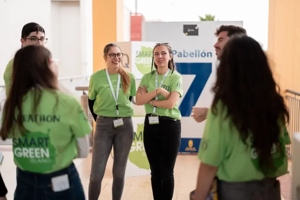 Eine Gruppe von Menschen in grünen „Smart Green“-T-Shirts steht in einem Flur und unterhält sich in der Nähe eines Schilds mit der Aufschrift „Pabellón 7“.